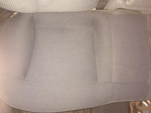 Fragment szarej, teksturowanej tapicerki kanapy z widocznymi śladami użytkowania i delikatnymi plamami.