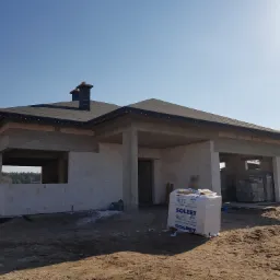 Niedokończony, parterowy dom murowany z dachem pokrytym papą, widoczne bloczki Solbet na palecie