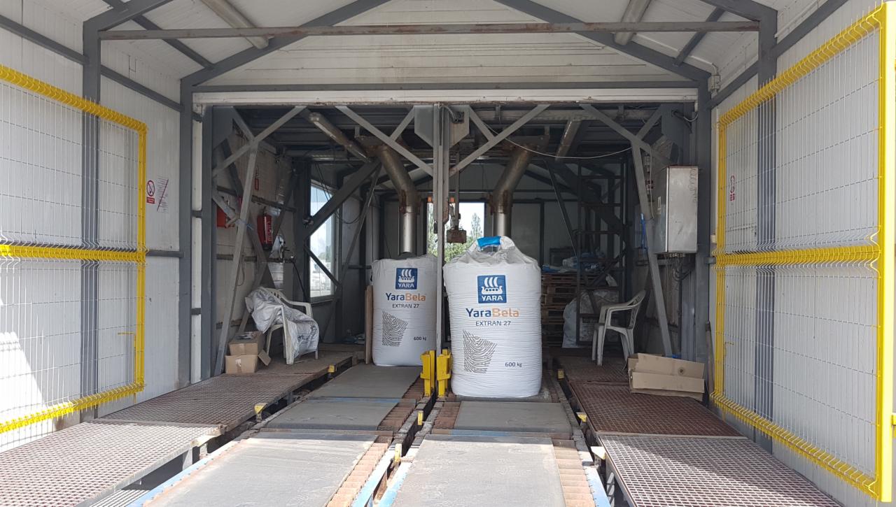 Dwa worki nawozu YaraBela Extran 27 o wadze 600 kg ustawione na platformach w hali produkcyjnej z metalowymi konstrukcjami i żółtymi barierkami ochronnymi.