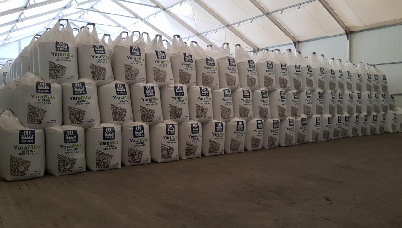 Rzędy ułożonych worków z nawozem YaraMila Viking NPK 14-14-21 w magazynie z białym dachem namiotowym.