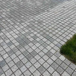 Ułożona pod kątem nawierzchnia z szarej kostki w Krakowie, widoczny fragment trawnika w prawym dolnym rogu.