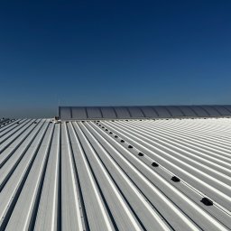 Eektro-Instal lewków - Biały, blaszany dach przemysłowy z zamontowaną instalacją odgromową na tle błękitnego nieba.