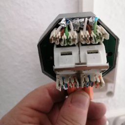 Eektro-Instal lewków - Szczegółowe ujęcie rozdzielnicy elektrycznej z podłączonymi przewodami o różnych kolorach, trzymanej w dłoni na tle białej ściany z gniazdkami.