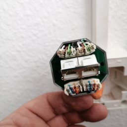 Eektro-Instal lewków - Otwarta puszka instalacyjna z widocznymi złączami kablowymi i przewodami w różnych kolorach, trzymana w dłoni na tle białej ściany.