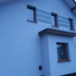 Nowoczesna elewacja domu jednorodzinnego w odcieniach błękitu z poziomymi pasami w górnej części, widoczne okna z brązowymi ramami i fragment dachu.