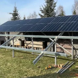 Montaż paneli słonecznych na konstrukcji wsporczej w ogrodzie, widoczne narzędzia i elementy instalacji.