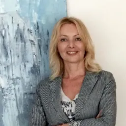 Portret uśmiechniętej blondynki w marynarce, na tle abstrakcyjnego obrazu w biurze w Warszawie. Profesjonalny wizerunek pracownika biura.