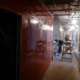 Spektor Plus - Korytarz w trakcie prac wykończeniowych, ściana pokryta czerwoną, błyszczącą farbą, widoczne drabiny i pracownicy w oddali.