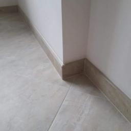 Spektor Plus - Wykończony narożnik pomieszczenia z beżowymi płytkami podłogowymi i listwami przypodłogowymi, widoczne połączenie płytek i listew przy ścianie.