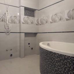 Spektor Plus - Wanna z mozaiką w łazience z białymi płytkami z motywem róży, widoczne przygotowane otwory na armaturę, przewody zwisające ze ściany.