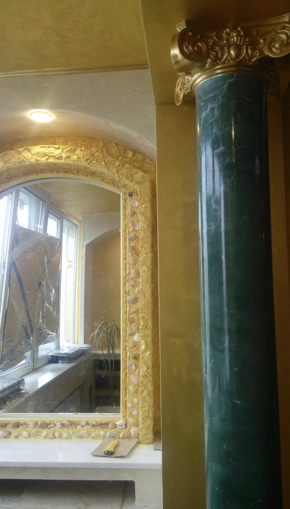 Bogato zdobione wnętrze z kolumną z zielonego marmuru, łukiem z dekoracjami w kolorze złota i wkomponowanymi muszelkami, widok na okno z zabezpieczeniem folią.