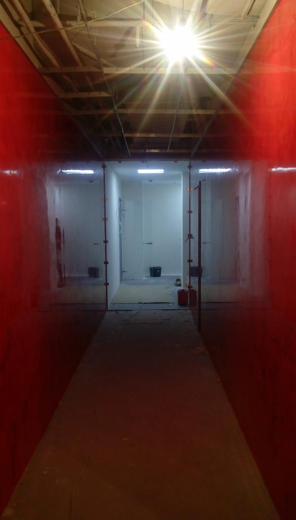 Wnętrze w trakcie remontu, ściany częściowo pomalowane na czerwono, w tle widoczne płyty gipsowo-kartonowe i akcesoria malarskie.