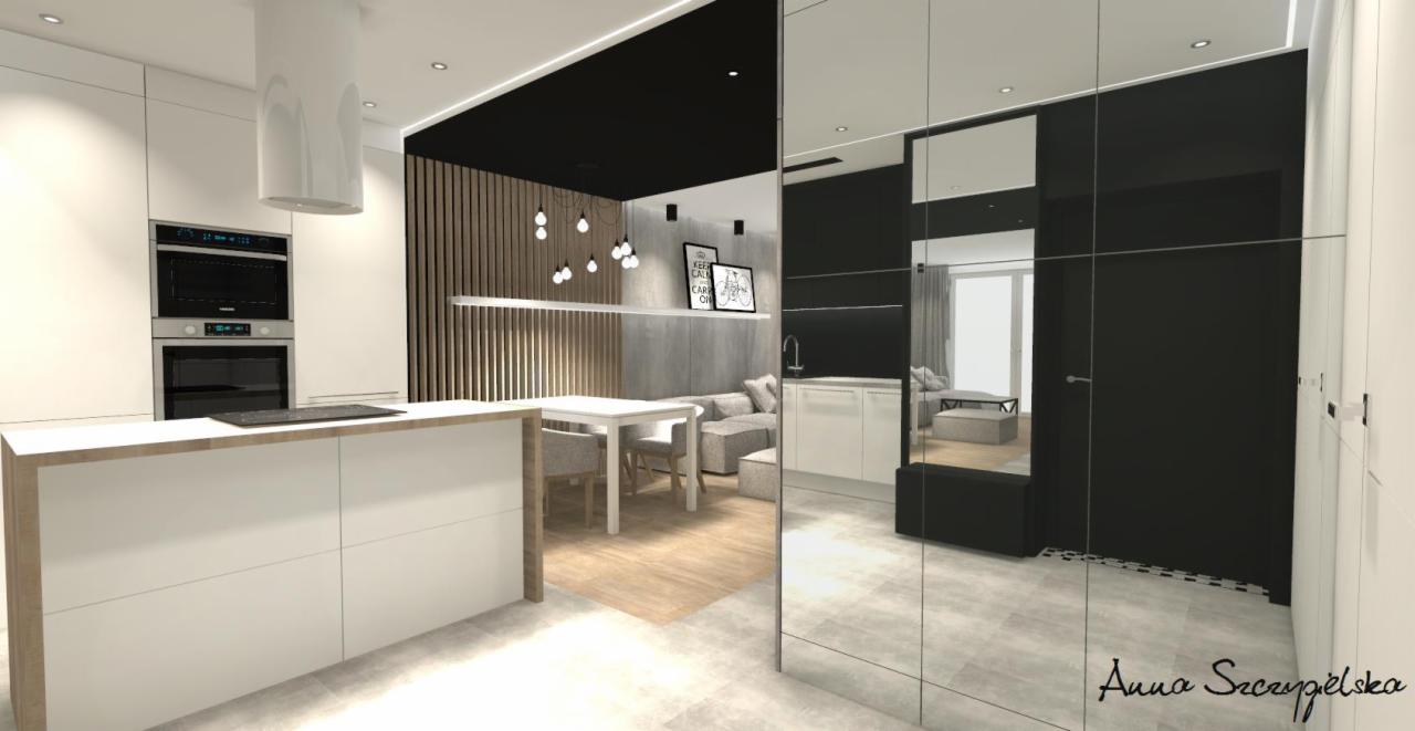 Wizualizacja wnętrza: nowoczesna kuchnia z wyspą i zabudową, widok na salon z drewnianymi lamelami i szarą sofą, odbicie w lustrzanej szafie, podpis projektanta w prawym dolnym rogu.