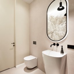 Rynkowski Design - Nowoczesna łazienka w beżowej tonacji z wiszącą toaletą, umywalką wolnostojącą i podświetlanym lustrem owalnym.