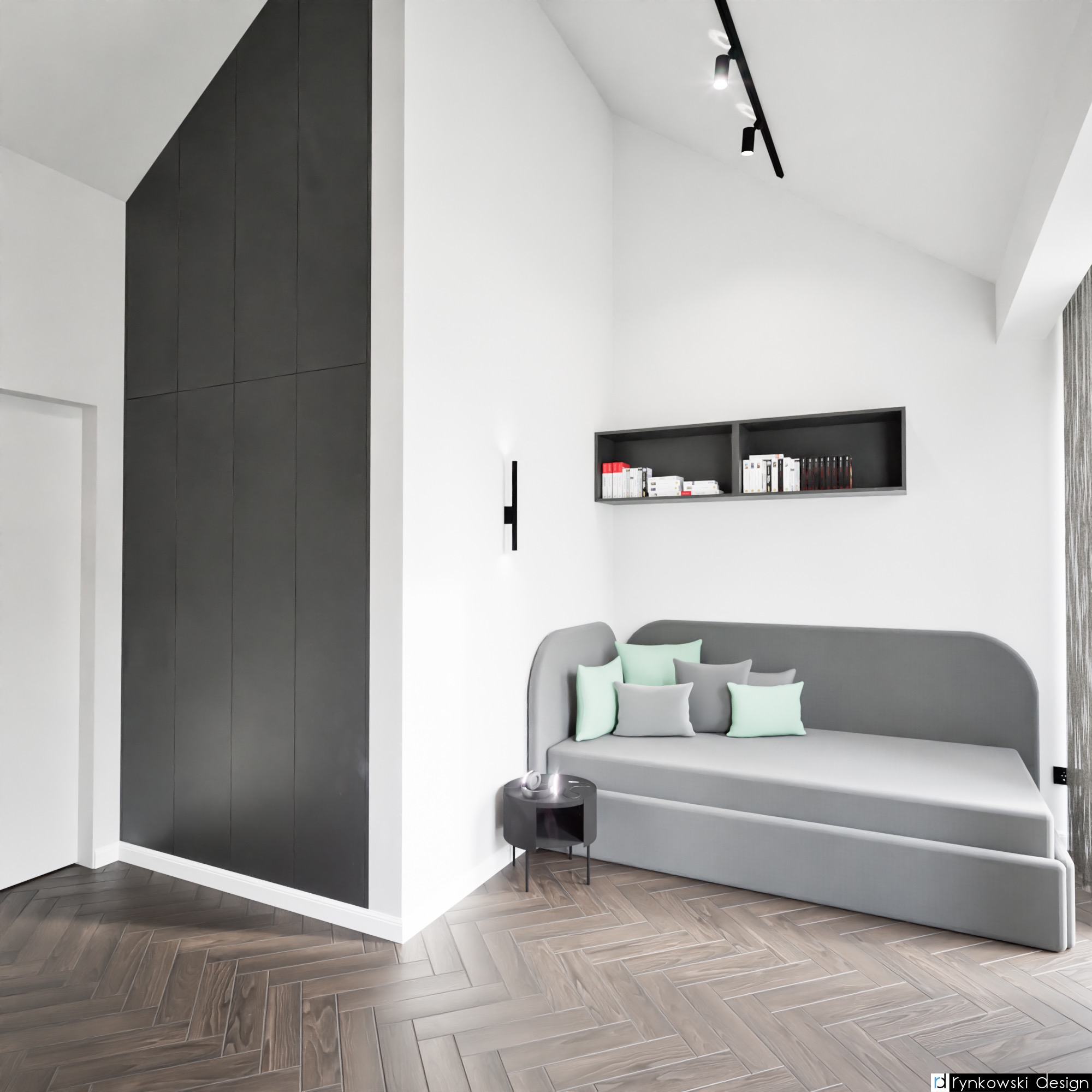 Minimalistyczny pokój z szarą sofą, pastelowymi poduszkami, ciemnoszarą zabudową ścienną, parkietem w jodełkę i czarną półką na książki.