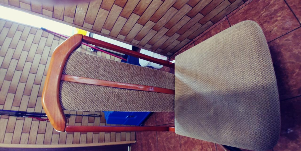 Krzesło z drewnianą ramą i beżową tapicerką, widziane z góry, na tle brązowych płytek podłogowych i sufitowych w Wejherowie.