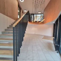 Wnętrze nowoczesnego budynku z betonowymi schodami z drewnianymi stopniami i czarną balustradą, oświetlone wiszącą lampą z żarówkami w stylu retro.