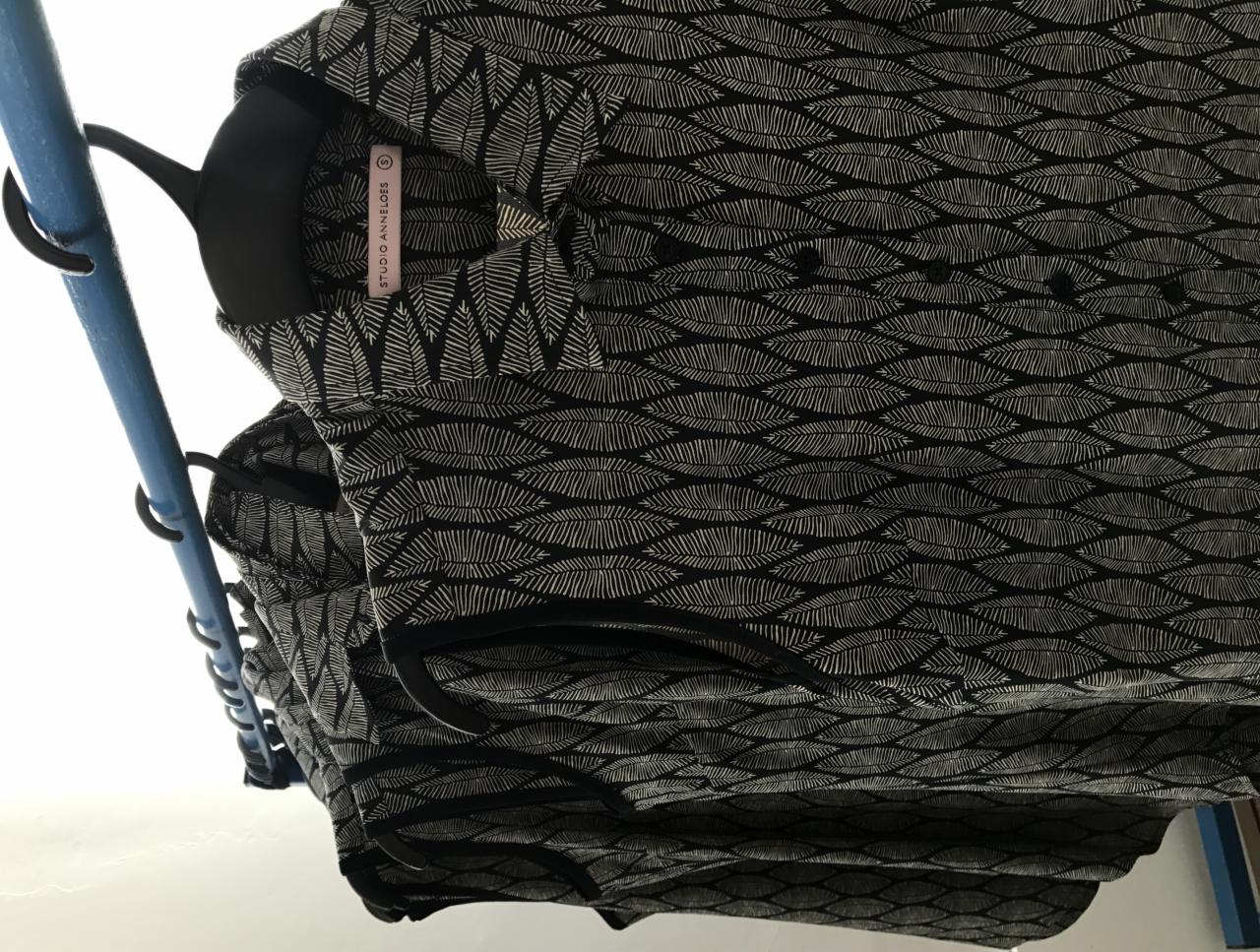 Czarno-biała bluzka z motywem liści na wieszaku, widoczna metka 'Studio Anneloes'.