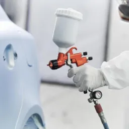 Pracownik w kombinezonie ochronnym lakieruje element karoserii samochodu za pomocą pistoletu natryskowego w warsztacie w Chomranicach.