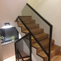 Stalmar - Drewniane schody z czarną, metalową balustradą z siatki, oświetlone światłem z okna z roślinami. Nowoczesny design, widok z góry.