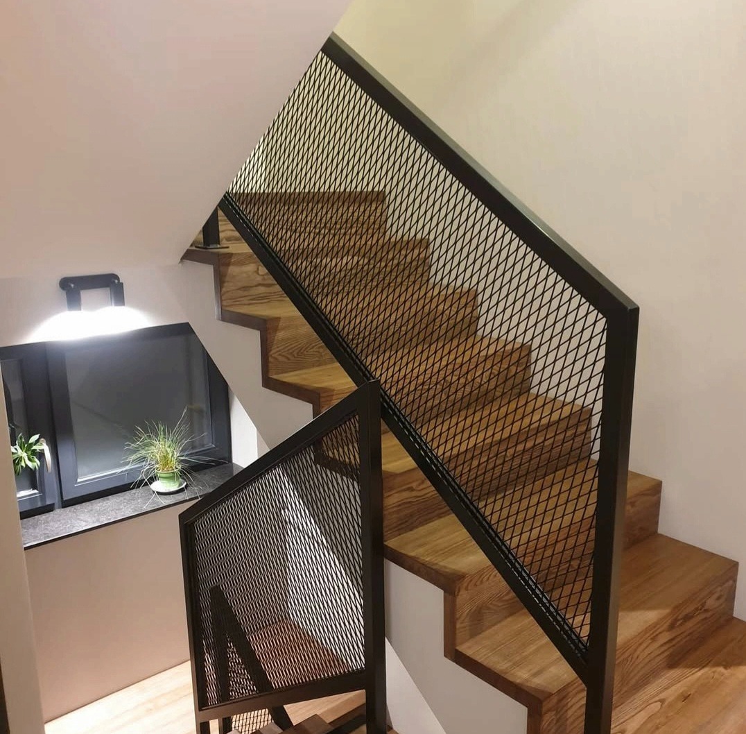 Drewniane schody z czarną, metalową balustradą z siatki, oświetlone światłem z okna z roślinami. Nowoczesny design, widok z góry.