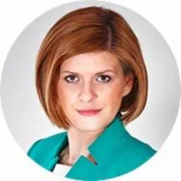 Portret kobiety z krótkimi, rudymi włosami, ubranej w zielony żakiet i białą bluzkę, na jasnoszarym tle w okręgu.