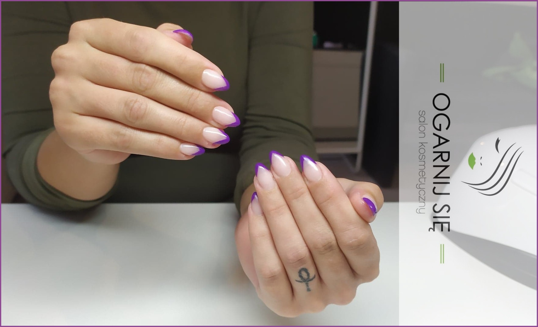Dłonie z geometrycznym manicurem french w odcieniach fioletu, na jednej dłoni widoczny tatuaż na palcu, w tle lampa UV i logo salonu kosmetycznego.