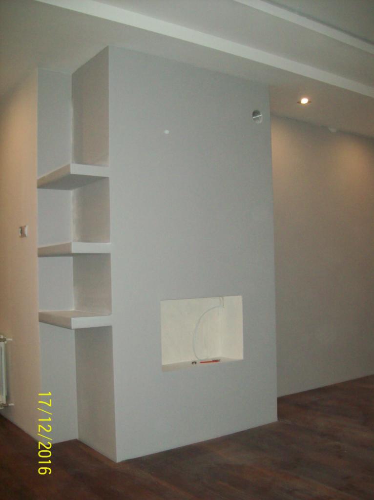 Szara ściana z wnękami i półkami po remoncie, widoczne kable w jednej z wnęk, podłoga z paneli.