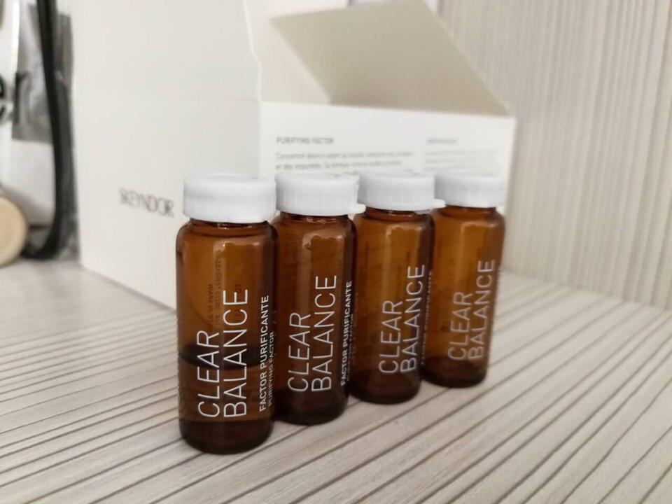 Cztery brązowe buteleczki z białymi zakrętkami marki Skeyndor Clear Balance, ustawione w rzędzie na jasnym tle, widoczne opakowanie zbiorcze