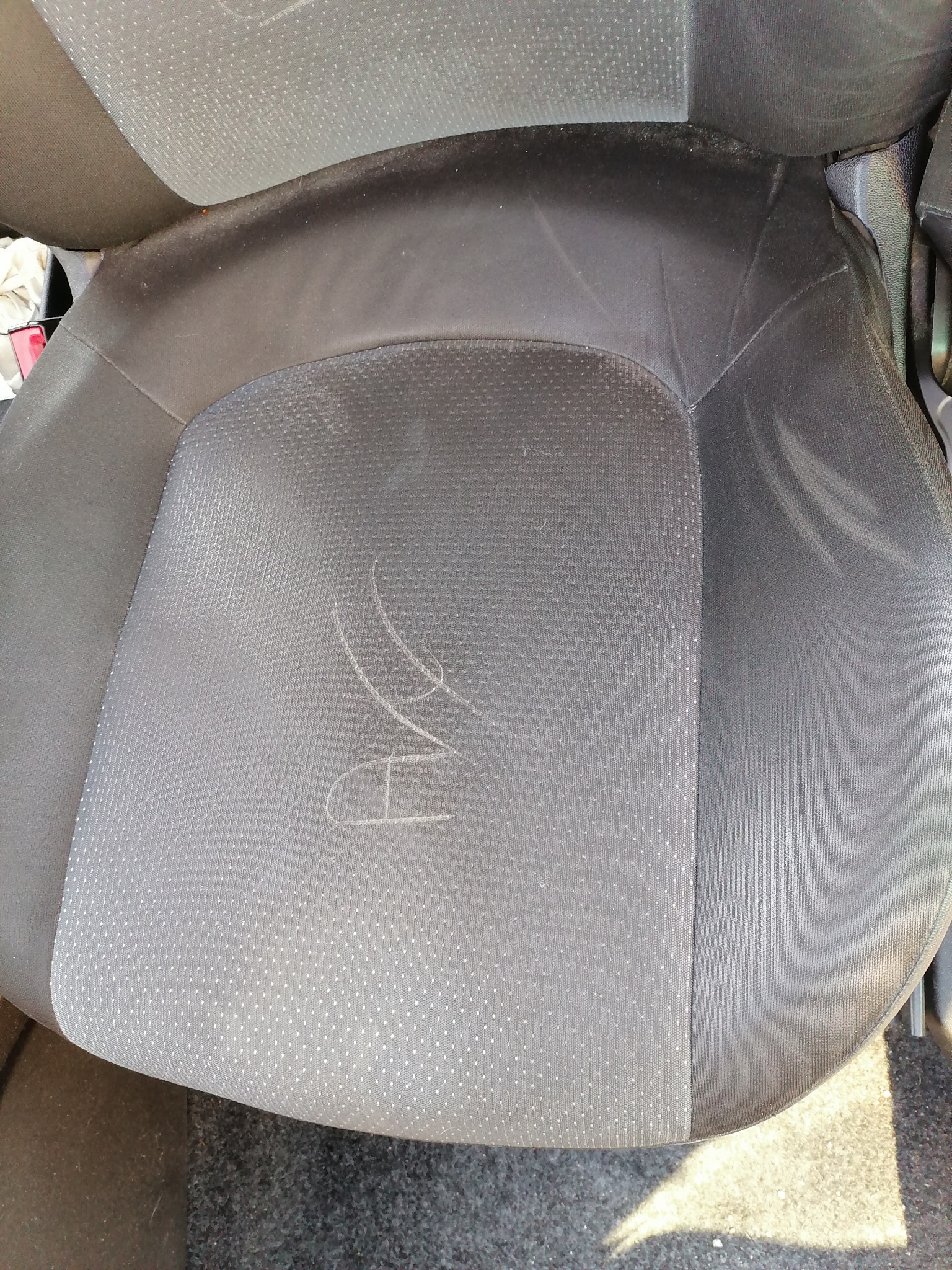 Brudne, czarne siedzenie samochodowe z widocznymi plamami i zarysowaniami na powierzchni tapicerki.