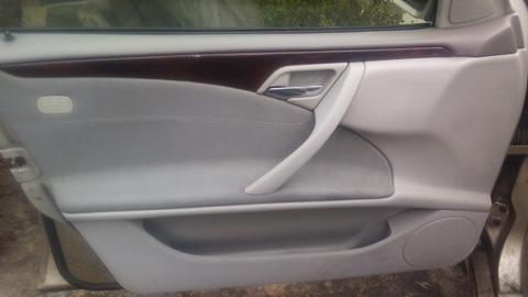 Wnętrze drzwi samochodowych z szarą tapicerką i drewnianym wykończeniem, widoczny uchwyt i głośnik.