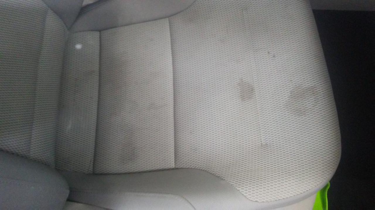 Szare tekstylne siedzenie samochodowe z widocznymi plamami przed czyszczeniem.