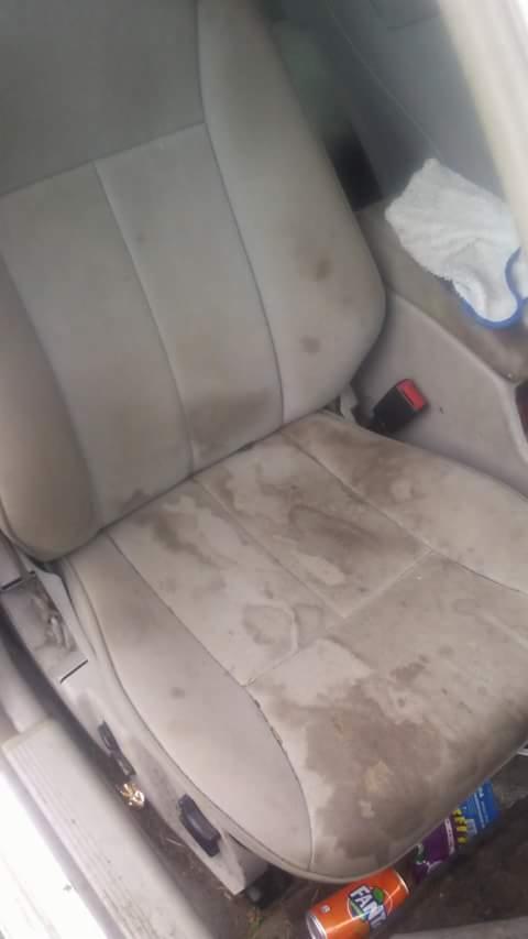 Bardzo zabrudzone, jasne, materiałowe siedzenie samochodowe z widocznymi plamami, obok leży puszka po napoju i chusteczka