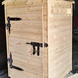 Konstrukcje drewniane Kamil Hewig - Surowa, drewniana wędzarnia z czarnymi okuciami, umieszczona na palecie, widoczne otwory wentylacyjne i proste zapięcie, tło warsztatowe.