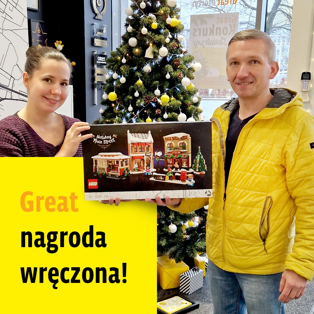 Dwie osoby prezentują nagrodę - zestaw LEGO Holiday Main Street na tle świątecznej choinki i prezentów, z żółtym banerem z tekstem 'Great nagroda wręczona!'