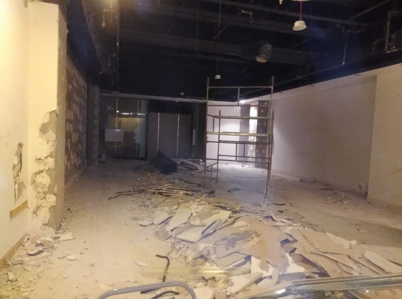 Wnętrze w trakcie demontażu, widoczne fragmenty usuniętej ściany, gruz na podłodze oraz metalowe rusztowanie.