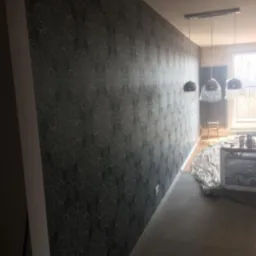 Ściana po tapetowaniu w pokoju z widocznymi lampami wiszącymi i grzejnikiem pod oknem.