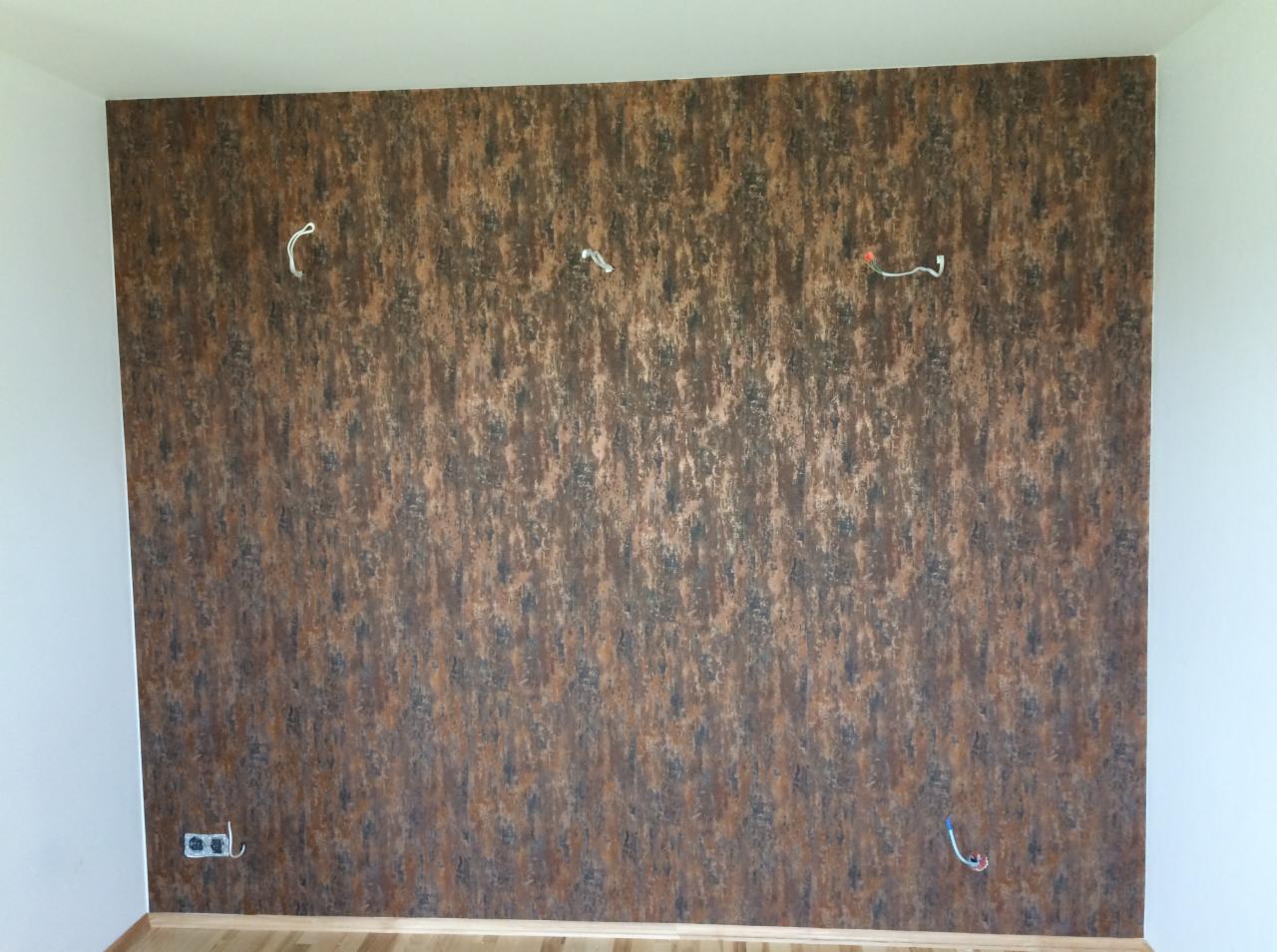 Ściana pokryta tapetą w odcieniach brązu i czerni, z widocznymi przewodami elektrycznymi wystającymi ze ściany.