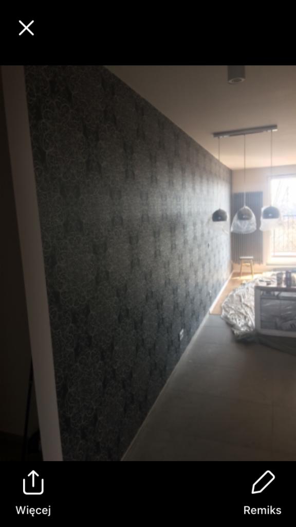 Ściana po tapetowaniu w pokoju z widocznymi lampami wiszącymi i grzejnikiem pod oknem.