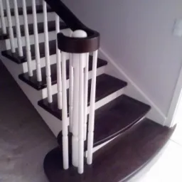 Fragment nowoczesnych schodów z ciemnego drewna z białymi balustradami i zaokrąglonym stopniem początkowym.