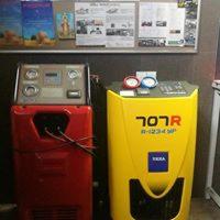 Dwa urządzenia do obsługi systemów klimatyzacji: czerwone i żółte, stojące obok siebie w warsztacie, z tablicą informacyjną w tle.