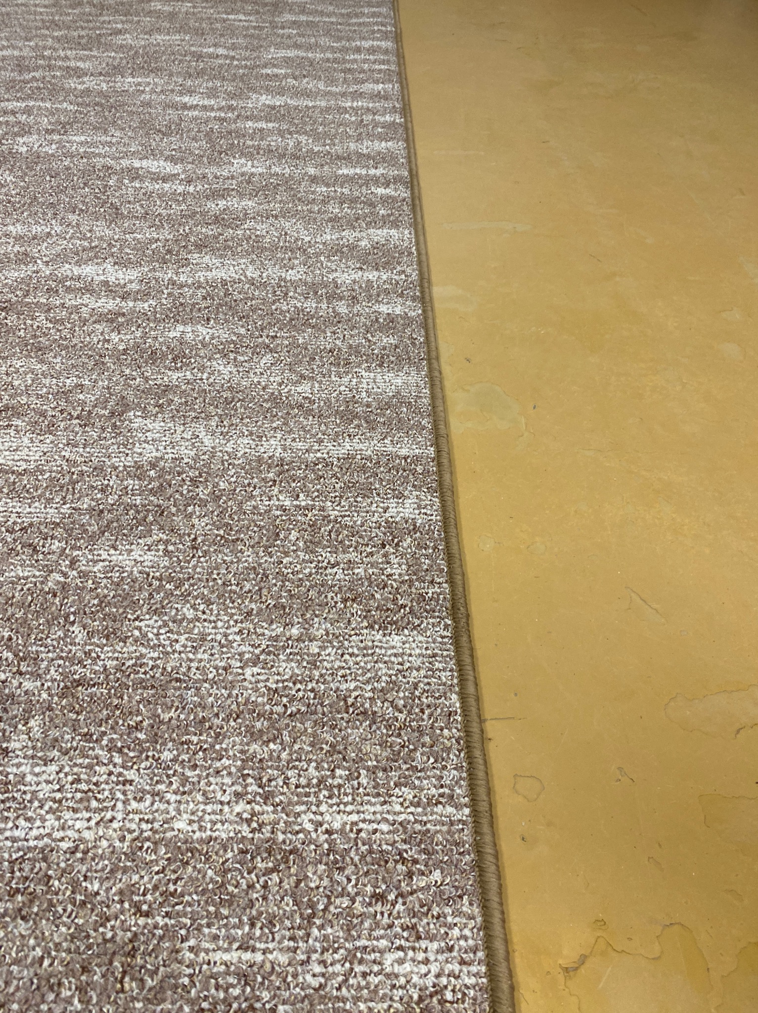 Fragment podłogi z nową, wzorzystą wykładziną dywanową, przylegającą do starej, żółtej powierzchni. Widoczny brzeg łączenia materiałów.
