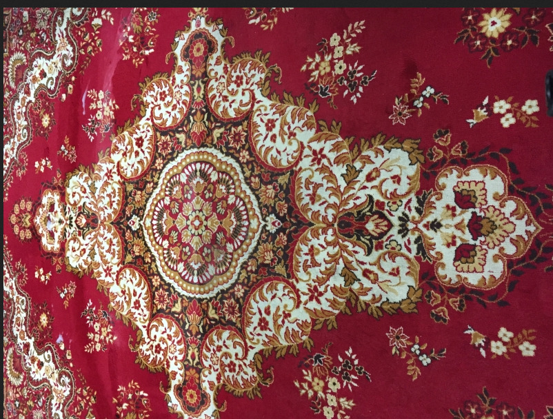 Czerwony dywan z bogatym, orientalnym wzorem w odcieniach bieli, złota i czerni, z widocznym śladem po czyszczeniu w centralnej części.