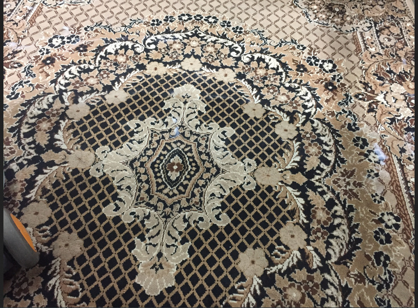 Wzór dywanu w odcieniach beżu, brązu i czerni z motywami kwiatowymi i geometrycznymi, widoczne ślady po czyszczeniu w postaci jaśniejszych plam.