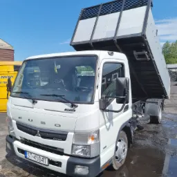 Biała wywrotka Fuso Canter z podniesioną skrzynią ładunkową, widoczna tablica rejestracyjna ST 4504T i odbicie w kałuży.