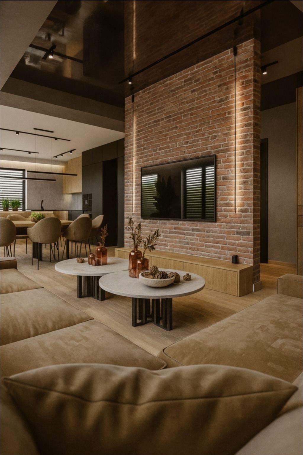 Salon z ceglaną ścianą, telewizorem i okrągłymi stolikami kawowymi. W tle jadalnia i kuchnia. Minimalistyczne oświetlenie sufitowe.