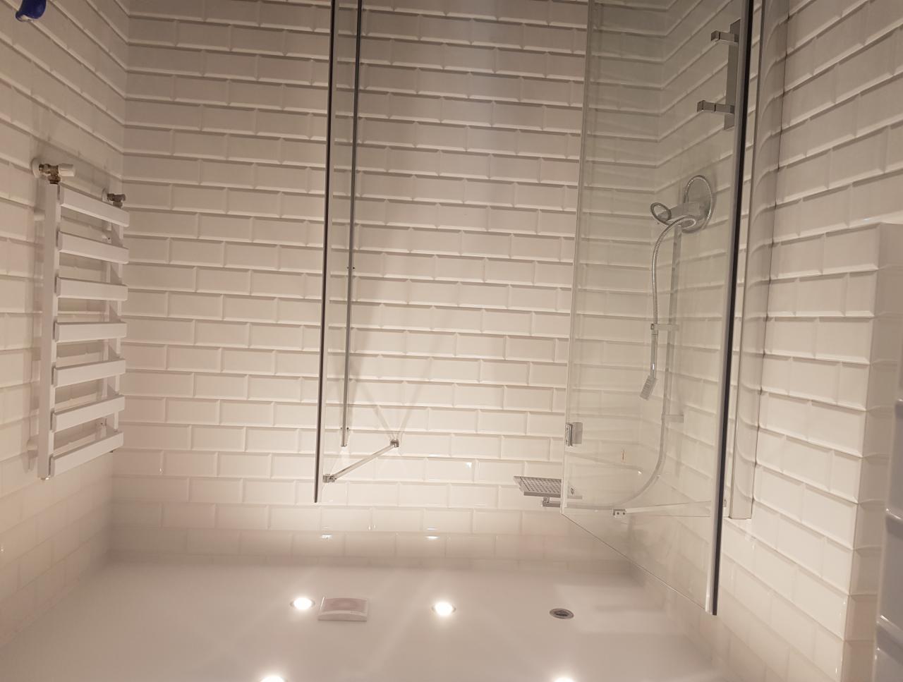 Biała łazienka z kabiną prysznicową typu walk-in wykończona płytkami imitującymi cegłę, z grzejnikiem drabinkowym po lewej stronie.