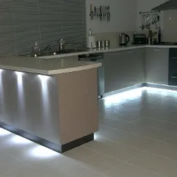 Nowoczesna kuchnia z podświetleniem LED szafek w Białymstoku, tworzącym unikalny efekt wizualny na białej podłodze z płytek.