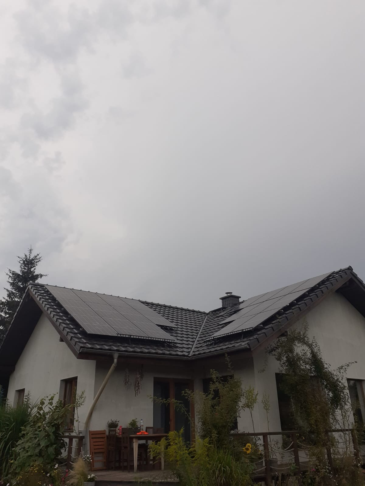 Dom jednorodzinny z panelami fotowoltaicznymi na dachu pokrytym ciemną dachówką, widok z dołu w pochmurny dzień.