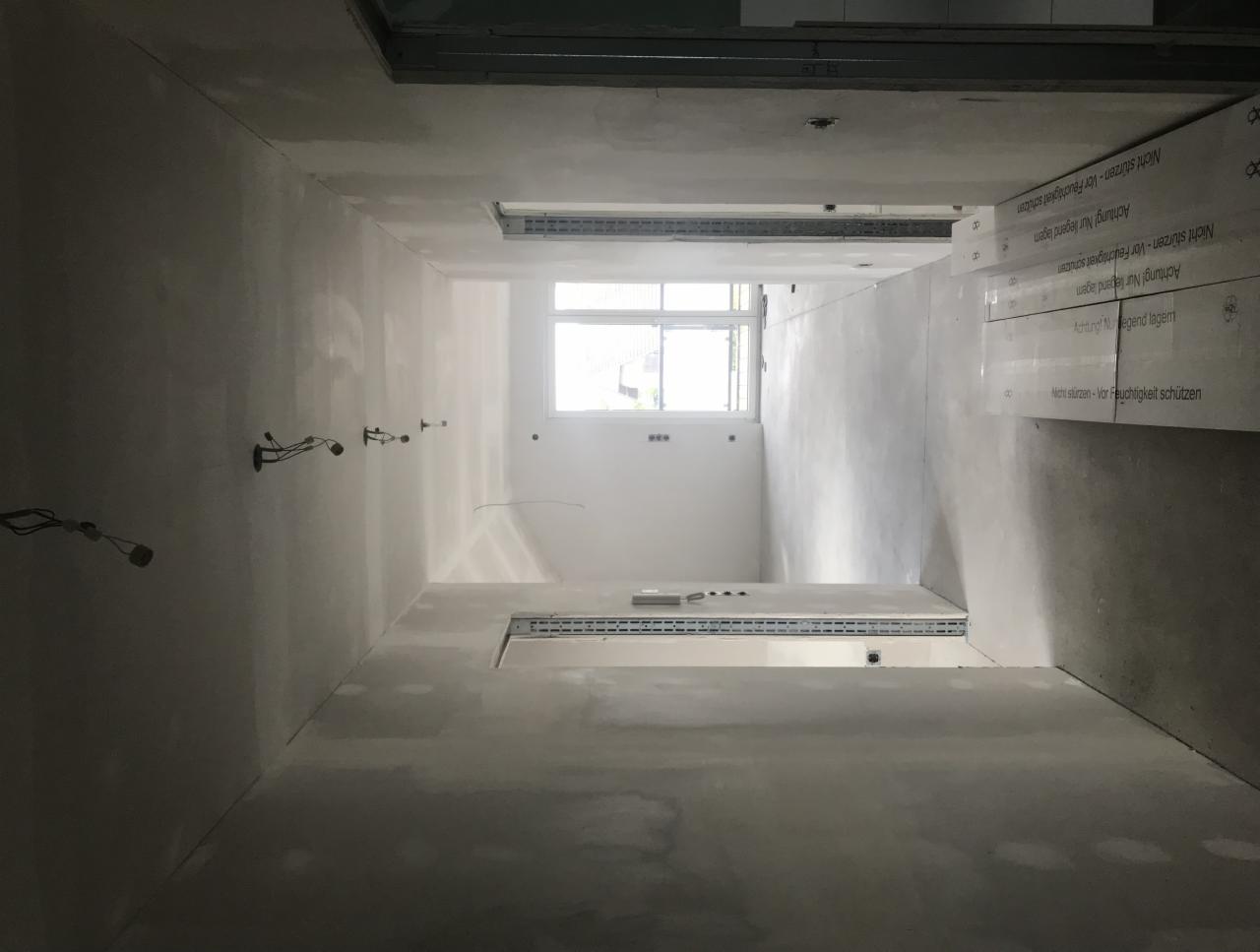 Wnętrze w trakcie prac wykończeniowych, widoczne ściany po szpachlowaniu, wystające przewody elektryczne i ułożone płyty kartonowo-gipsowe przy suficie.